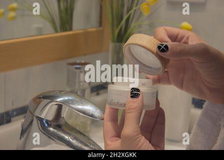 Young male hand in bathrobe holding face cream to apply after shaving. Beauty Home Spa Concept. Stock Photo
