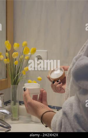 Young male hand in bathrobe holding face cream to apply after shaving. Beauty Home Spa Concept. Stock Photo