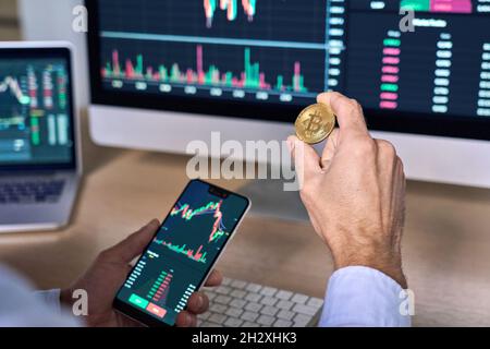 Cypto trader investor holding phone and coin buying bitcoin using mobile app. Stock Photo