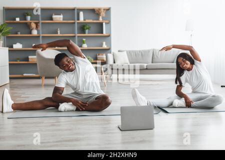 Young black couple doing side bend exercise using pc Stock Photo