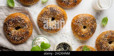 Variety fresh whole-grain bagels with poppy seeds, sesame seeds and ingredients for breakfast on a light concrete or stone background. Selective focus Stock Photo