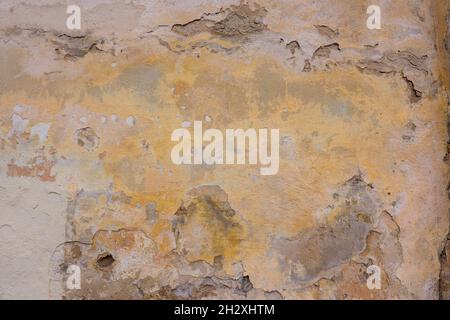 Old cracked weathered shabby yellow painted plastered peeled wall background. Chipped broken uneven rough stucco wall texture wallpaper Stock Photo
