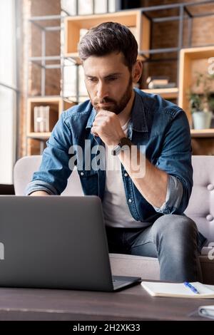 Concentrated man reading information and checking data working online on laptop Stock Photo