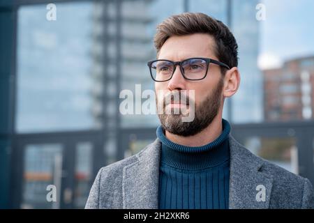 Portrait of pensive businessman in eyeglasses looking aside standing outdoors Stock Photo