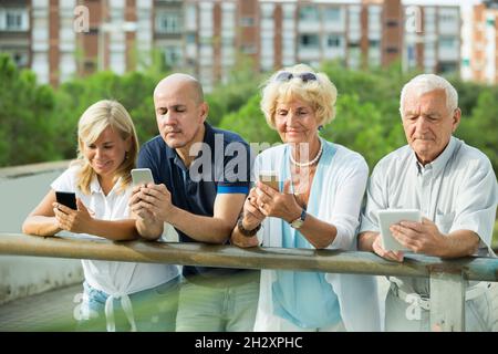 Smiling mature couples using gadgets in park Stock Photo
