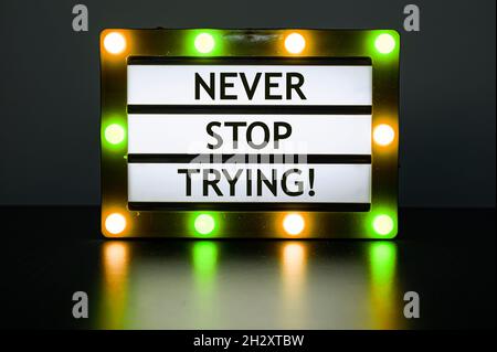 Lightbox with orange and green lights in dark room with words - never stop trying. Stock Photo