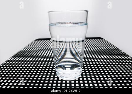 A glass on a square holed black lattice creating peculiar distortion patterns. Triangle shape with imploded sides in the center. Stock Photo