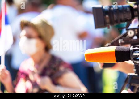 TV reporting during COVID-19 pandemic, blurred person with face mask in the background Stock Photo