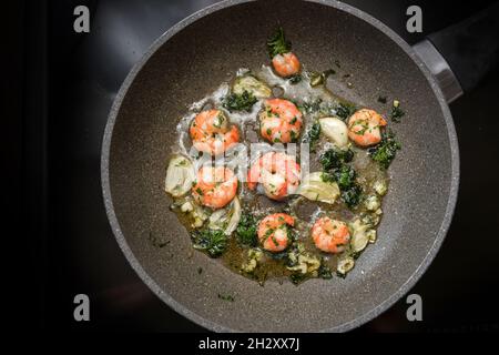 Frying pan with shrimps or black tiger prawns sauteed with olive oil, garlic and parsley on a black stove, cooking mediterranean,  delicious seafood s Stock Photo