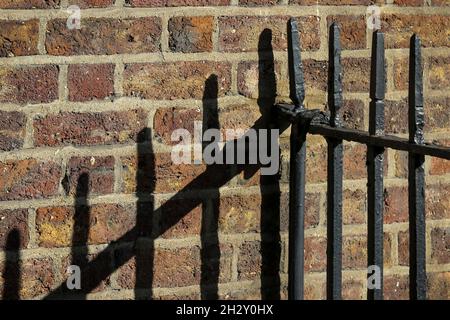 Black iron railings cast linear shadows or lines onto old stone brick wall. Dublin, Ireland Stock Photo