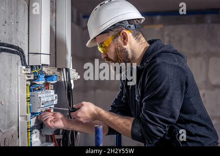 A male electrician works in a switchboard with an electrical connecting cable. Stock Photo