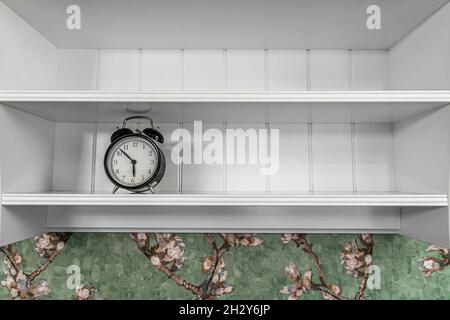 Classic vintage alarm clock on the shelf in the interior of the room. Stock Photo