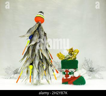 christmas tree decorated with fishing lures This Christmas tree is made of dried fish. New year for the fisherman. The  tree is decorated with floats and fishing tackle. A boot with sweets near t  Stock Photo