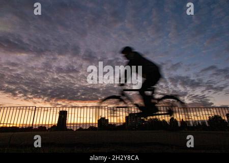 A cyclist rides through a London park at sunset with a tower block in the distance Stock Photo