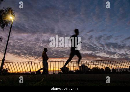Running as the sun sets in an urban park in London with a tower block in the distance Stock Photo