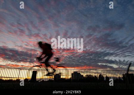 A cyclist rides through a London park at sunset with a tower block in the distance Stock Photo