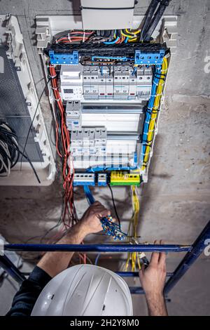 A male electrician works in a switchboard with an electrical connecting cable. Stock Photo
