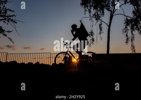 A cyclist rides through a London park at sunset with a tower block in the distance Stock Photo