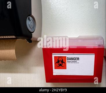 Red biohazard sharps waste container mounted to the wall of a public restroom Stock Photo