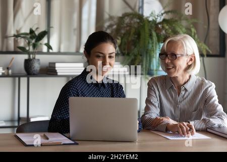 Old age female employee discuss project with young indian colleague Stock Photo