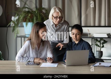 Two multiethnic females students listen to experienced mature woman teacher Stock Photo
