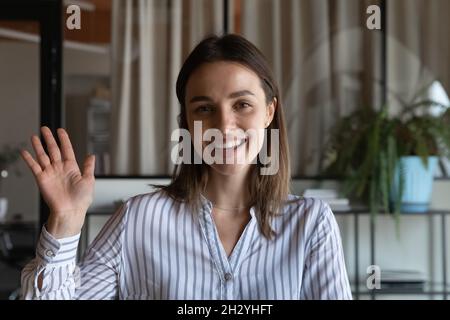 Screen portrait of smiling female presenter wave hand to camera Stock Photo