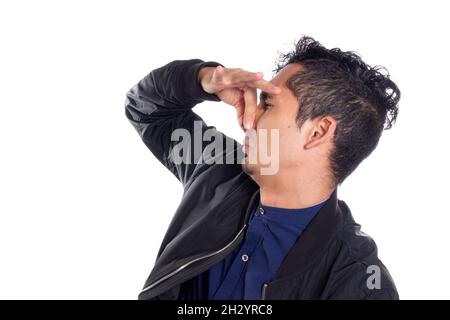 Man holding his nose because of bad odor. White background. Young adult latino man with disgusted expression of bad smell. Stock Photo