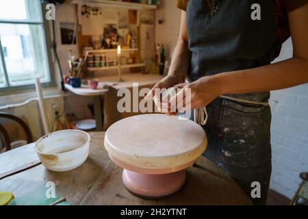 Pottery artist female molding clay on wheel. Ceramist in apron work with raw earthenware for potter Stock Photo