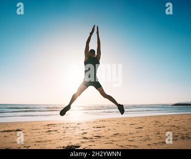 Jumping man. Young fitness man doing jumping jacks or star jump exercise on the beach Stock Photo