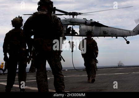U.S. Marines with Maritime Raid Force, 22nd Marine Expeditionary Unit (MEU), conduct fast rope drills from a MH-60S Seahawk aboard the amphibious dock landing ship USS Gunston Hall (LSD 44), Oct. 21, 2021. LSD 44, a support vessel for the 22nd MEU and Amphibious Squadron (PHIBRON) 6, is underway for PHIBRON-MEU Integrated Training (PMINT) in preparation for future deployment. PMINT is the first at-sea period in the MEU’s Redeployment Training Program; it aims to increase interoperability and build relationships between Marines and Sailors. (U.S. Marine Corps photo by Sgt. Mason Roy) Stock Photo