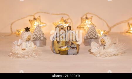 christmas festive scenery showing the Holy Family with 2 handcrafted angel ornaments in warm golden light; front view with blurred bokeh star lights Stock Photo