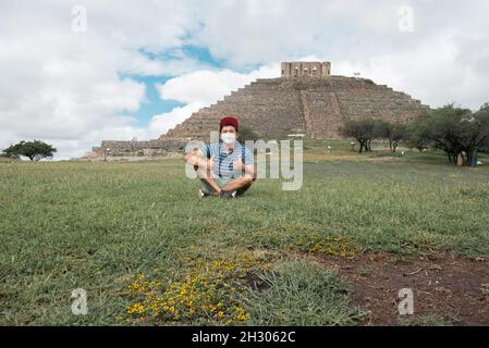 young hispanic, mexican, latino man, sitting in a green field with the pyramid of el pueplito in querétaro de fonod, archaeological site, tourist dest Stock Photo