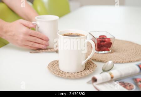 woman serving a coffee in a white light kitchen using eco knit jute tablemats. good morning concept. crop view Stock Photo