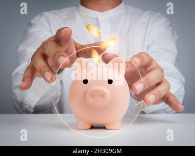 Financial management concept. Pink piggy bank with golden money coins and operation icon symbol, businessman with magical touch on white table. Saving Stock Photo