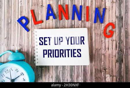 Alarm clock and notepad with text. Prioritize on a wooden background. Planning written in wooden letters Stock Photo
