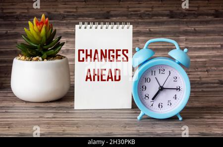 CHANGES AHEAD Concept is written on a notebook. Alarm clock and cactus stand on a wooden table. Stock Photo