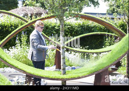 Gardener waters the World Vision Garden at the RHS Hampton Court Palace Flower Show, at Hampton Court, Teddington in London.  Stock Photo