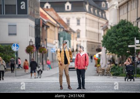 Young man with Down syndrome and his mentoring friend walking and talking outdoors Stock Photo