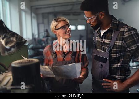 Portrait of young biracial industrial colleagues working indoors in metal workshop, smiling. Stock Photo