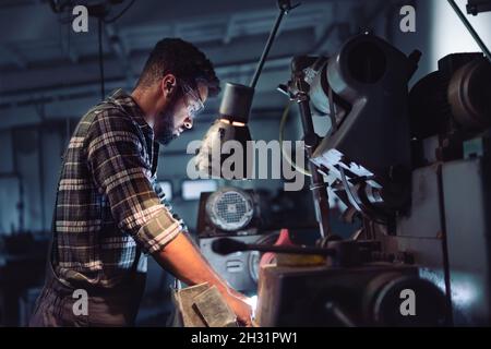 Portrait of young concentrated african american man working on cutter indoors in metal workshop. Stock Photo