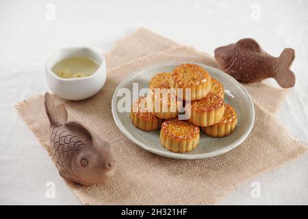 Traditional festive moon cake and cup of chamomile tea served for mid autum festival on table decorated with clay fishes Stock Photo