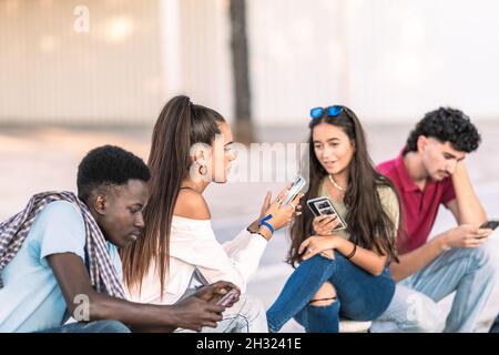 Group of multiracial students using the mobile phone while sitting outdoors Stock Photo