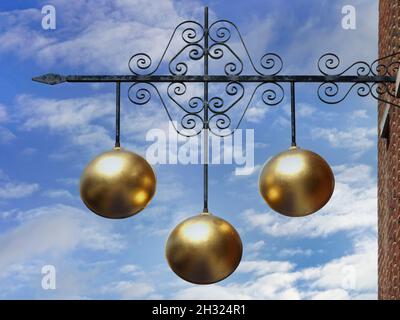 Pawn shop close up traditional sign three gold balls above Pawnbroker shop premises supported on ornamental iron bracket on a blue sky day England UK Stock Photo