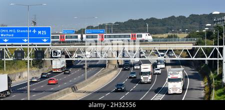 M25 motorway gantry signs railway bridge & Greater Anglia passenger train crossing above road traffic junction 28 for A12 Brentwood Essex England UK Stock Photo