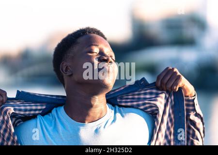 Young african man taking a sunbath while taking off the t-shirt outdoors Stock Photo