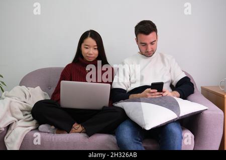 Young couple relaxing on a couch at home using laptop and smartphone. Stock Photo
