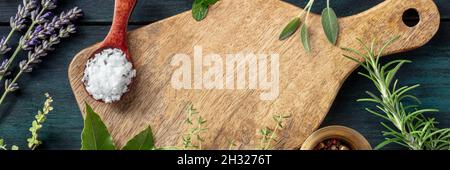 Cooking with herbs panorama. A wooden cutting board with salt and aromatic herbs. Lavender, rosemary, sage and bay leaf. Culinary design template Stock Photo