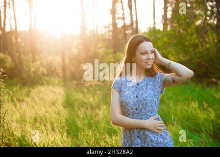 Beautiful girl in a blue summer dress in the rays of the sunset in the park. Stock Photo