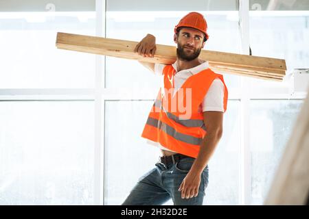 Builder man in hardhat carrying timber on building site, close up . Stock Photo