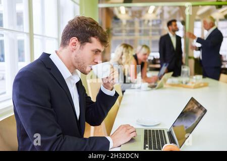 Young business man drinking a cup of coffee during a break in the office at the computer Stock Photo